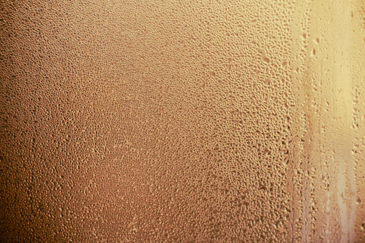 A detailed shot of dewdrops creating a pattern on a glass surface with warm lighting.