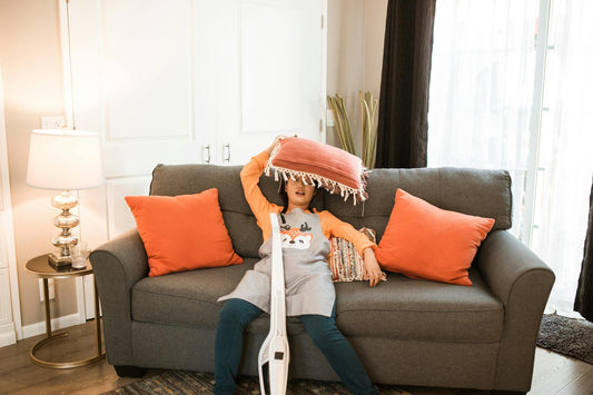 Young girl playing with pillows on a cozy couch indoors, surrounded by warm decor.