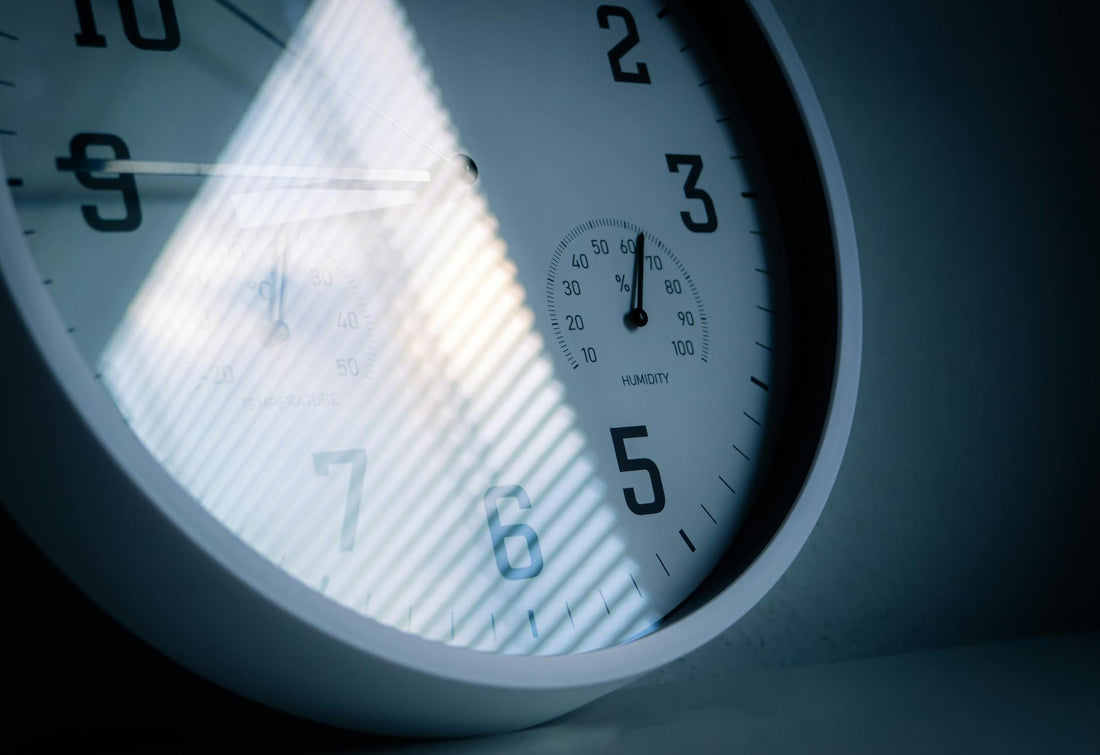 A close-up of a wall clock showing time and humidity, reflecting light and shadows.