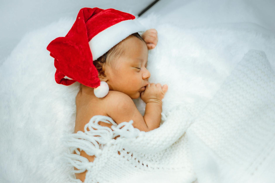 Cute newborn baby wearing a Santa hat and sleeping peacefully in soft white blankets.