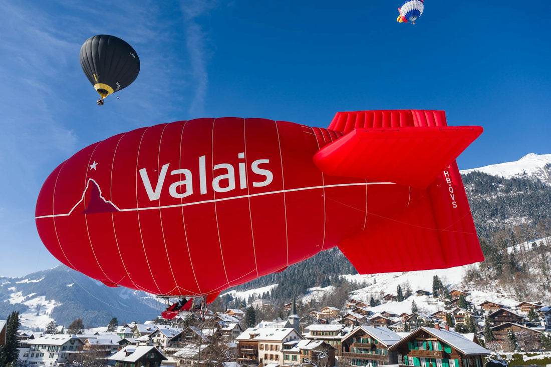 Hot air balloons soar over a scenic Swiss village, showcasing vibrant colors against a winter landscape.