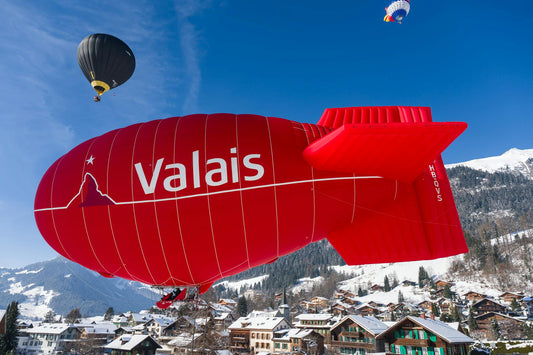 Hot air balloons soar over a scenic Swiss village, showcasing vibrant colors against a winter landscape.