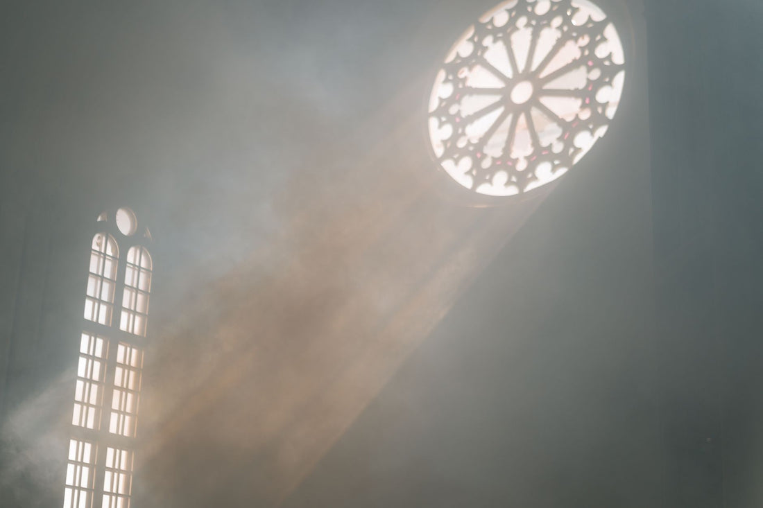 Sunlight streams through ornate church windows, casting beams into a dusty interior.